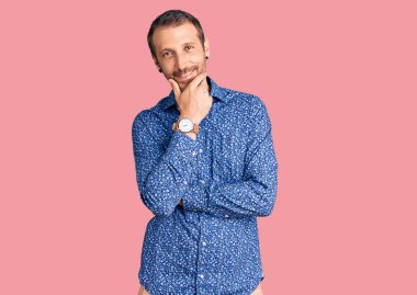 Sıradan kıyafetler giyen, kameraya kendinden emin, kolları çapraz ve çenesi havada gülümseyen genç yakışıklı bir adam. Olumlu düşünmek. 