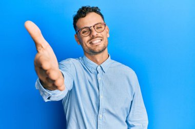 Gündelik giysiler ve gözlük takan genç İspanyol adam gülümseyen, yardım eli uzatan ve kabul gören biri.. 