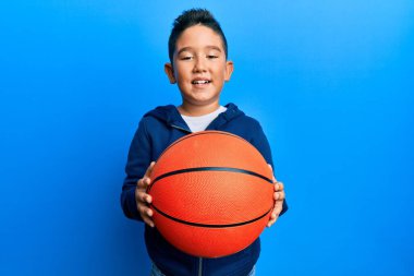 Basketbol topu tutan küçük İspanyol çocuk kameraya seksi bir ifadeyle bakıyor, neşeli ve mutlu bir yüzle.. 