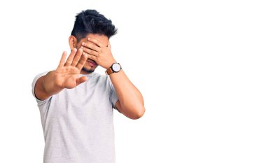 Yakışıklı Latin Amerikalı genç adam gündelik tişörtler giyip gözleri ellerle kapatıyor ve üzgün ve korku ifadeleriyle jestleri durduruyor. utangaç ve olumsuz kavram. 