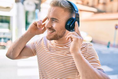 Genç İrlandalı gülümseyen mutlu müzik dinleyen şehir caddesinde kulaklık kullanan.