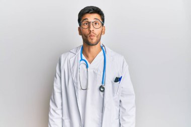 Doktor üniforması ve steteskop giyen genç yakışıklı adam dudaklarıyla balık suratı yapıyor, çılgınca ve komik bir jest. Komik ifade. 