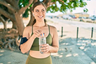 Genç sarışın sporcu şehirde bir şişe su içerek egzersiz yapıyor..