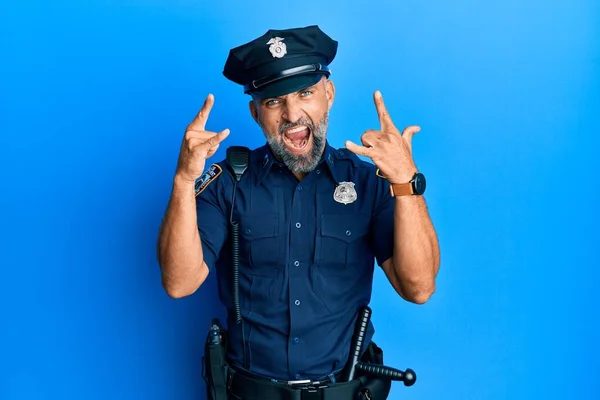 Middle age handsome man wearing police uniform shouting with crazy expression doing rock symbol with hands up. music star. heavy music concept.