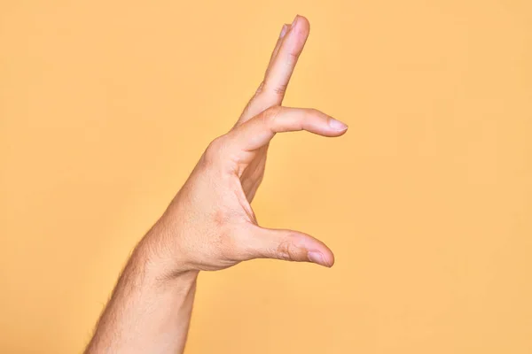 孤立した黄色の背景のピッキングの上に指を示す白人の若者の手と目に見えないものを取ります 空間を示す指でオブジェクトを保持 — ストック写真