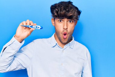 Genç İspanyol adam termometreyi tutuyor. Korkmuş ve ağzı açık kalmış, şaşırmış ve şaşırmış. 