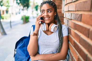 Genç Afro-Amerikan öğrenci kız gülümsüyor. Üniversite kampüsünde akıllı telefondan mutlu bir şekilde konuşuyor.