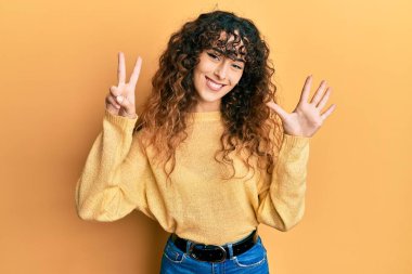 Gündelik kıyafetler giyen genç İspanyol kız yedinci parmaklarını gösterip işaret ederken kendinden emin ve mutlu bir şekilde gülümsüyor.. 