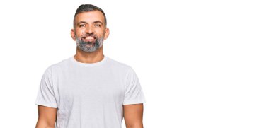 Yüzünde mutlu ve havalı bir gülümseme olan sıradan beyaz tişört giyen orta yaşlı yakışıklı bir adam. şanslı kişi. 