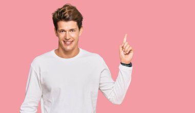 Yakışıklı beyaz süveter giyen, yüzünde kocaman bir gülümseme olan, eli kameraya bakan beyaz bir adam.. 