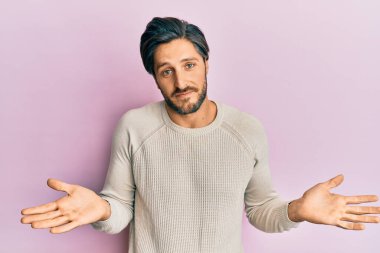 Sıradan bir kazak giyen, elleri ve kolları havada, kafası karışmış genç İspanyol bir adam. şüphe kavramı. 