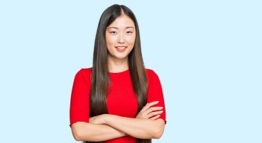 Sıradan kıyafetler giyen genç Çinli kadın kollarını kavuşturup kameraya bakarken gülümsüyor. pozitif kişi. 