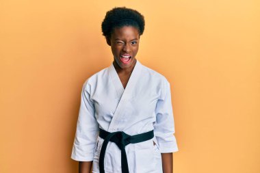 Genç Afrikalı Amerikalı kız karate kimonosu giyiyor ve siyah kuşak takıyor. Kameraya seksi bir ifadeyle bakıyor, neşeli ve mutlu bir yüzle.. 