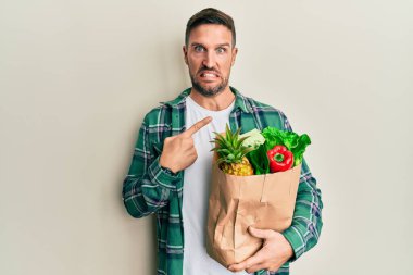 Elinde poşet sakallı yakışıklı bir adam. Elinde alışveriş torbası var. Endişeli ve endişeli. 