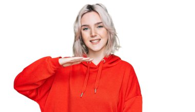 Genç sarışın kız, sıradan kıyafetler giyiyor. Elleriyle işaret ediyor. Büyük ve büyük beden işareti, ölçü işareti. Kameraya bakıp gülümsüyor. ölçüm kavramı. 