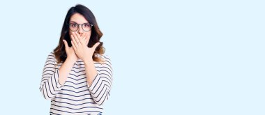 Gündelik giysiler ve gözlük takan güzel, genç esmer kadın yanlışlıkla elleriyle ağzını kapatarak şok etti. gizli kavram. 