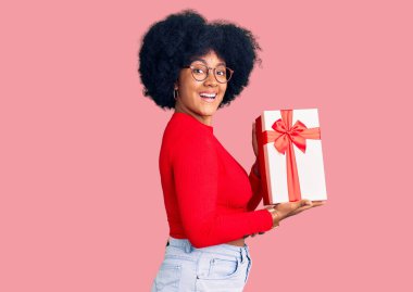 Genç Afro-Amerikalı kız elinde hediyeyle avuç içi açık bir şekilde fotokopi alanını gösteriyor, gülümseyerek mutlu bir gülümseme sunuyor. 