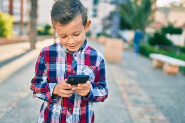 Beyaz çocuk şehirde akıllı telefon kullanarak mutlu bir şekilde gülümsüyor..