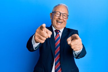 İş elbisesi giyen ve kravat takan kıdemli beyaz adam parmaklarıyla sana ve kameraya bakıyor, gülümsüyor ve neşeli. 