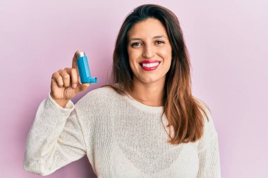 Güzel İspanyol kadın elinde astım spreyi tutuyor. Pozitif ve mutlu görünüyor. Kendine güvenen bir gülümsemeyle dişlerini gösteriyor. 