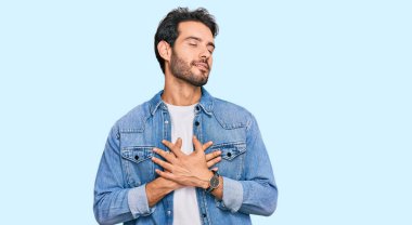 Gündelik kıyafetler giyen genç İspanyol adam elleri göğsünde, gözleri kapalı ve yüzünde minnet dolu bir jest ile gülümsüyor. sağlık kavramı. 