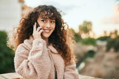 Genç İspanyol kadın gülümsüyor. Şehirdeki akıllı telefondan konuşuyor.