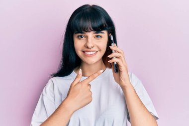 Genç İspanyol kız akıllı telefondan konuşuyor. Gülümsüyor. Elinle ve parmağınla işaret ederek mutlu ol. 