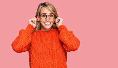 Güzel sarışın kadın günlük kıyafetler ve gözlük takıyor gülümsüyor kulakları parmaklarıyla çekiyor, komik bir jest. deneme sorunu 