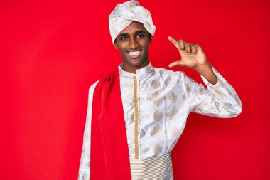 Geleneksel Sherwani elbisesi giyen yakışıklı Hintli adam gülümseyen ve kendine güvenen el hareketleriyle küçük beden işareti yapan parmakları ve kamerayla bakan. ölçüm kavramı. 