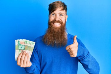 Genç İrlandalı kızıl adam Hong Kong 'u tutuyor 50 dolarlık banknotlar gülümsüyor mutlu ve olumlu, başparmak yukarı, mükemmel ve onay işareti yapıyor. 