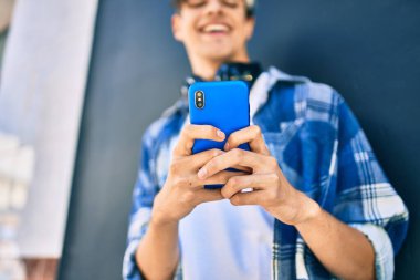 Genç İspanyol adam şehirde akıllı telefon ve kulaklık kullanarak mutlu gülümsüyor..