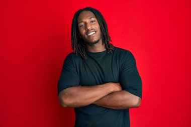 Saçları örgülü, mutlu yüzlü, kollarını kavuşturup kameraya bakan Afro-Amerikan bir adam. pozitif kişi. 