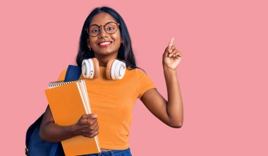 Sırt çantası ve kitapları tutan genç Hintli kız bir fikir ya da soruyla şaşırdı ve mutlu yüzle işaret etti. 