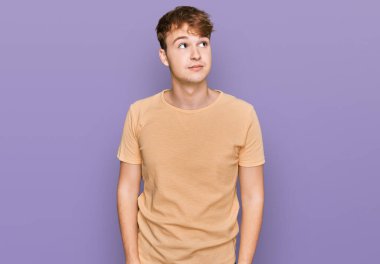 Gündelik giysiler giymiş genç beyaz bir adam gülümseyip yan tarafa bakıyor ve düşünüyor.. 