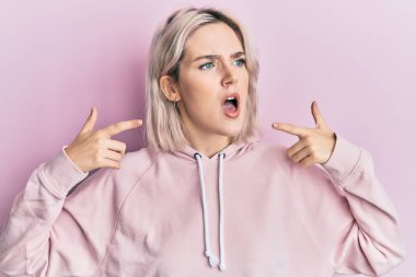 Genç sarışın kız kızgın ve kızgın parmaklarıyla dudaklarını göstererek sinirli ve öfkeli çığlıklar atıyor, öfkeyle bağırıyor. öfke ve agresif konsept. 