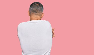 Orta yaşlı, beyaz tişört giyen yakışıklı bir adam mutlu ve pozitif bir şekilde kendini kucaklıyor. Sevgi ve özgüven. 