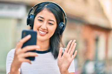 Genç İspanyol kadın şehirde akıllı telefon ve kulaklık kullanarak video görüşmesi yapıyor..