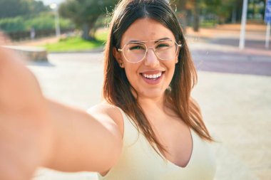 Mutlu gülümseyen genç ve güzel bir kadın. Yüzünde tebessümle dikilip şehrin caddesindeki kameranın önünde selfie çekiyorum..