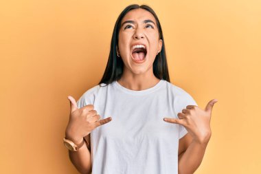 Genç Asyalı kadın elleriyle shaka işareti yapıyor. Kızgın ve kızgın çığlıklar atıyor. Öfkeyle bağırıyor.. 