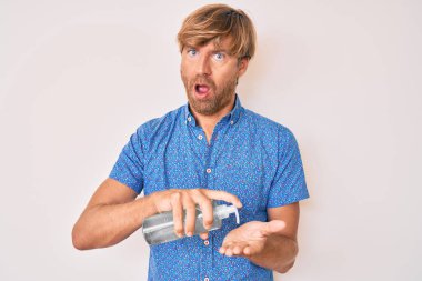 Sarışın genç adam şok edici yüzüne el dezenfektanı sürüyor. Şüpheci ve alaycı görünüyor. 