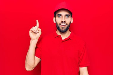 Sakallı, polo giyen ve şapkalı genç yakışıklı bir adam bir fikir veya soruyla gülümsüyor ve mutlu bir yüzle işaret ediyor. 