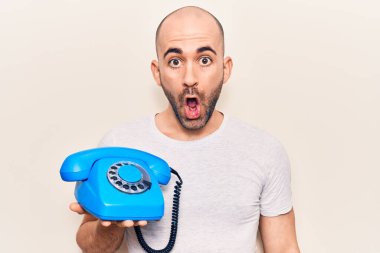 Kel ve yakışıklı bir adam elinde klasik bir telefon tutuyor. Korkmuş ve ağzı açık kalmış, şaşırmış ve şaşırmış bir halde. 