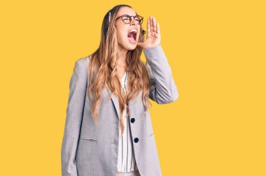 Çağrı merkezi kulaklığı takan genç ve güzel sarışın kadın el ve ağızla bağırarak ve yüksek sesle bağırıyor. iletişim konsepti. 