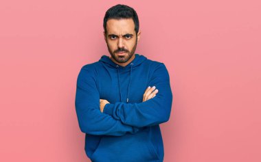 Gündelik kıyafetler giyen, kuşkucu ve gergin genç İspanyol bir adam. Yüzünde çapraz kollarla onaylamayan bir ifade var. negatif kişi. 