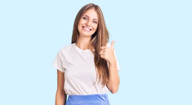 Yaz stili giyinen genç, güzel sarışın kadın elleriyle mutlu bir jest yapıyor. Kameraya bakıp başarıyı gösteren ifade. 