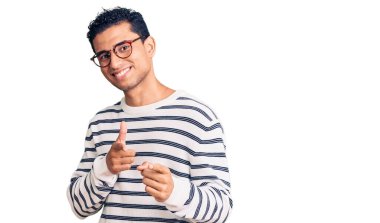 Gündelik kıyafetler giyen ve gözlüklü yakışıklı genç adam mutlu ve komik yüzlü parmaklarını kameraya doğrultuyor. iyi enerji ve titreşimler. 