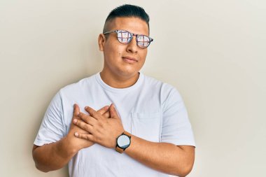 Gündelik kıyafetler ve gözlük takan genç latin adam elleri göğsünde gülümseyen, gözleri kapalı, yüzünde minnet ifadesi olan. sağlık kavramı. 