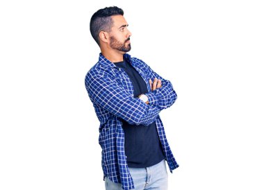 Sıradan kıyafetler giyen genç İspanyol adam kollarını kavuşturmuş ve kendinden emin bir şekilde yan tarafa bakıyor. 