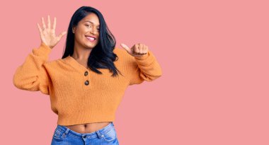 Uzun saçlı İspanyol kadın sıradan bir kazak giyiyor. Altıncı parmaklarını gösterip gülümsüyor. Kendinden emin ve mutlu.. 