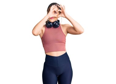 Güzel beyaz kadın spor kıyafetleri giyiyor ve kulaklık takıyor. El ve parmaklarıyla kalp şekli yapıyor. İşaretten bakıp gülümsüyor. 